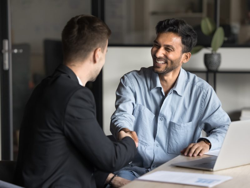 Cheerful,Multiethnic,Male,Business,Partners,Shaking,Hands,At,Workplace,Table,